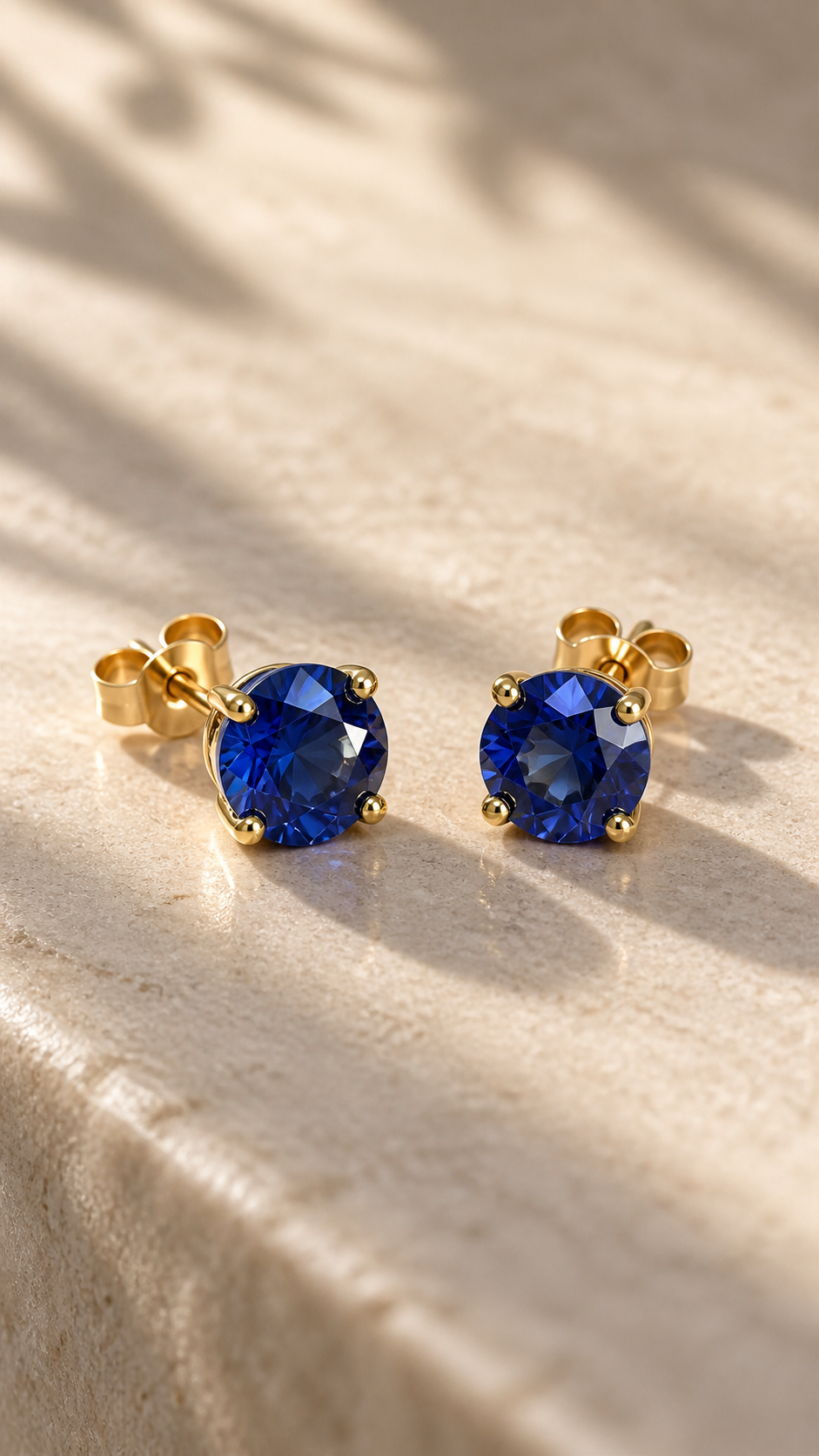 Athena blue sapphire studs on pale stone in soft olive-leaf shadows