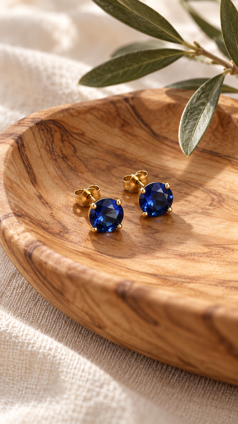 Athena blue sapphire studs in an olive wood dish beside an olive branch