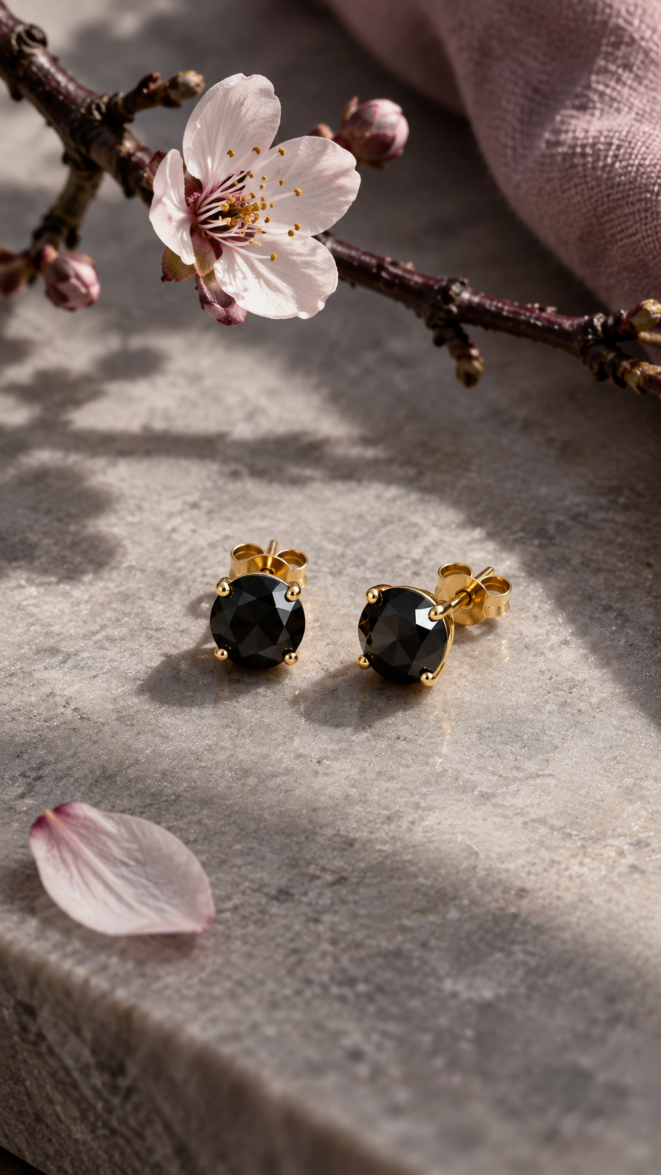 Persephone black moissanite studs on pale stone beneath a flowering branch